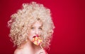 Beautiful fashionable blonde girl in retro style with voluminous curly hairstyle, open shoulders on a red background looks at the Royalty Free Stock Photo