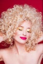 Beautiful fashionable blonde girl in retro style with voluminous curly hairstyle, open shoulders on a red background smiles with Royalty Free Stock Photo