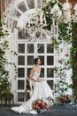 Beautiful and fashionable brunette model girl in stylish wedding dress with naked shoulders and with diadem on her head sits on th Royalty Free Stock Photo