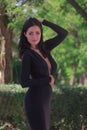 beautiful fashionable brunette woman adult posing in the park on the plants backgraund in black dress with a cleavage Royalty Free Stock Photo