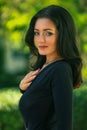 beautiful fashionable brunette woman adult posing in the park on the plants backgraund in black dress with a cleavage Royalty Free Stock Photo