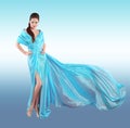 Beautiful fashionable Girl in blowing blue dress. Woman in Flying Gown, Silk Fabric Waving on Wind isolated on studio background. Royalty Free Stock Photo