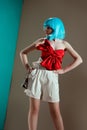 beautiful fashionable girl in blue wig and red bow standing with hands on waist and looking away Royalty Free Stock Photo