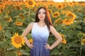 A beautiful fashionable girl with red hair stands in a rapeseed field in a dress, against a background of yellow flowers Royalty Free Stock Photo