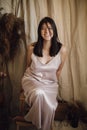 Beautiful fashionable happy woman in silk dress sitting in bohemian style room with dry grass