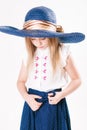 Beautiful fashionable little girl with blond hair in a hat with wide brim and a long fashionable skirt in the studio Royalty Free Stock Photo