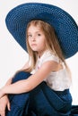 Beautiful fashionable little girl with blond hair in a hat with wide brim and a long fashionable skirt in the studio Royalty Free Stock Photo