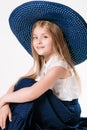 Beautiful fashionable little girl with blond hair in a hat with wide brim and a long fashionable skirt in the studio Royalty Free Stock Photo