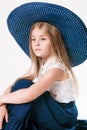 Beautiful fashionable little girl with blond hair in a hat with wide brim and a long fashionable skirt in the studio Royalty Free Stock Photo