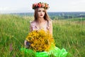 Beautiful fashionable pretty gorgeous girl in dress on the flowers field. Nice girl with wreath of flowers on her head and bouquet Royalty Free Stock Photo