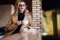 Beautiful fashionable stylish girl sits in a cafe with a cup of coffee. Royalty Free Stock Photo