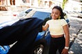Beautiful fashionable young african american woman posing in street against blue small city car. Fashion summer photo. Bright Royalty Free Stock Photo