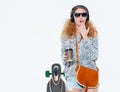 Beautiful fashionable young blond woman with a longboard, cup of coffee and cool headphones in surprise covers her mouth with her Royalty Free Stock Photo