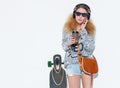 Beautiful fashionable young blond woman with a longboard, cup of coffee and cool headphones talking on the phone Royalty Free Stock Photo