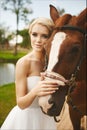 Beautiful and fashionable young bride, blonde model girl with blue eyes and stylish hairstyle in white dress posing with brown hor Royalty Free Stock Photo