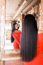 Beautiful fashionable young woman in beauty salon looking in mirror after makeup and hair care. Girl in red dress smiling, Royalty Free Stock Photo