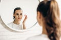 Beautiful female applying cosmetics on her face. Woman in bathroom applying cream on face