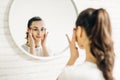 Beautiful female applying cosmetics on her face. Woman in bathroom applying cream on face