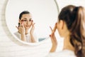 Beautiful female applying cosmetics on her face. Woman in bathroom applying cream on face