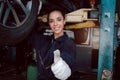 Beautiful female auto mechanic giving thumb up during checking wheel tires in garage, car service technician woman repairing Royalty Free Stock Photo
