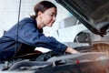 Beautiful female auto mechanic in uniform working with engine vehicle at garage, car service technician woman checking and Royalty Free Stock Photo