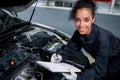 Beautiful female auto mechanic working in garage, car service technician woman holding file paper and checking car engine, Royalty Free Stock Photo