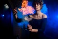 Beautiful female bartender holds glass with splashing drink, sprinkles and make fire over it. Royalty Free Stock Photo