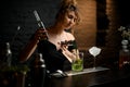 Beautiful female bartender professionally pours blue drink from jigger into cup.