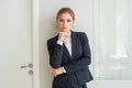Beautiful female blonde business woman CEO in a black suit at the workplace, standing confidently with arms folded Royalty Free Stock Photo