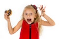 Beautiful female child with blue eyes in cute red dress eating chocolate donut with syrup stains Royalty Free Stock Photo