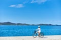 Woman riding a bicycle along stony sidewalk on blue sparkling sea water