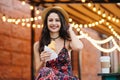 Beautiful female with dark hair, appealing appearance, wearing hat, dress and necklace, holding delicious croissant having cheerfu Royalty Free Stock Photo