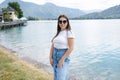 Beautiful female in denim skirt posing to photographer in front of big beautiful lake with clear water