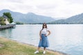 Beautiful female in denim skirt posing to photographer in front of big beautiful lake with clear water