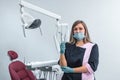 Beautiful female dentist standing in the dentistry near dental unit, holding medical tools and ready ready to accept a new patient