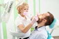 Beautiful female dentist wearing pink mask is attending the teeth of a young male client of modern dentistry