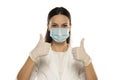 Beautiful female doctor or nurse wearing protective mask and latex or rubber gloves on white background with thumbs up Royalty Free Stock Photo