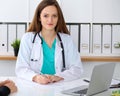 Beautiful female doctor and patient having a talk while sitting at the desk. Physician writes prescription with silver Royalty Free Stock Photo