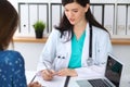 Beautiful female doctor and patient having a talk while sitting at the desk. Physician writes prescription with silver Royalty Free Stock Photo