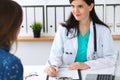 Beautiful female doctor and patient having a talk while sitting at the desk. Physician writes prescription with silver Royalty Free Stock Photo