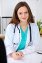 Beautiful female doctor and patient having a talk while sitting at the desk. Physician writes prescription with silver Royalty Free Stock Photo