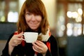 Beautiful female is drinking coffee in cafe. Mature woman with long hair looks at camera Royalty Free Stock Photo