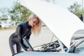 Beautiful female blonde driver repairs motor under car hood