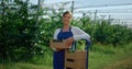 Beautiful female farmer looking camera near fresh fruit box at agrarian orchard.