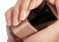 Beautiful female fingers with ideal naturel shiny beige manicure holding nail polish bottle. Care about female hands, healthy soft Royalty Free Stock Photo