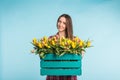 Beautiful female gardener holding box with tulips on blue background