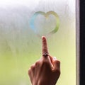 A beautiful female hand draws heart on misty window. finger on the wet glass draws the heart, window and rain Royalty Free Stock Photo