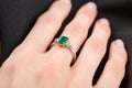 Beautiful female hand with gold ring with diamonds and emerald on gray background