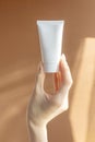 Beautiful female hand holding mock-up of white plastic cream tube in rays of sunlight. Container for professional Royalty Free Stock Photo