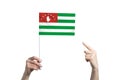 A beautiful female hand holds a Abkhazia flag to which she shows the finger of her other hand, isolated on white